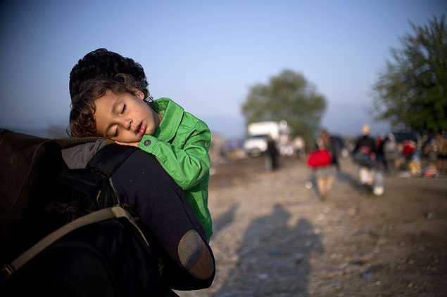 TOPSHOTS A migrant carrying his sleeping child crosses the Greek-Macedonian border near the town of Gevgelija on September 17, 2015. The European Parliament backed plans to relocate 120,000 refugees around the EU to help the frontline states of Greece, Hungary and Italy, in a move that hiked pressure on ministers to adopt the proposals next week. AFP PHOTO / NIKOLAY DOYCHINOV ORG XMIT: NIK001