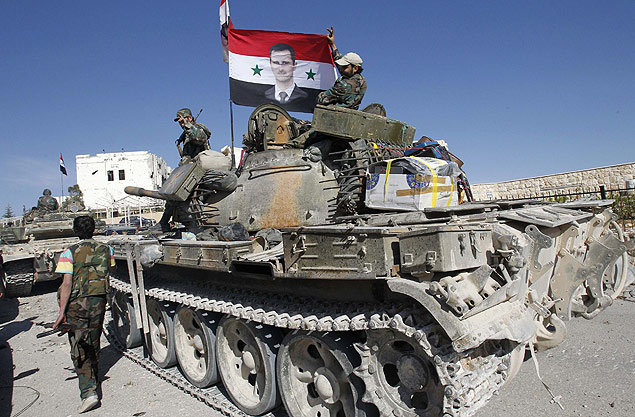 Soldados leais a Bashar al-Assad carregam bandeira sria com a foto do ditador em tanque de guerra