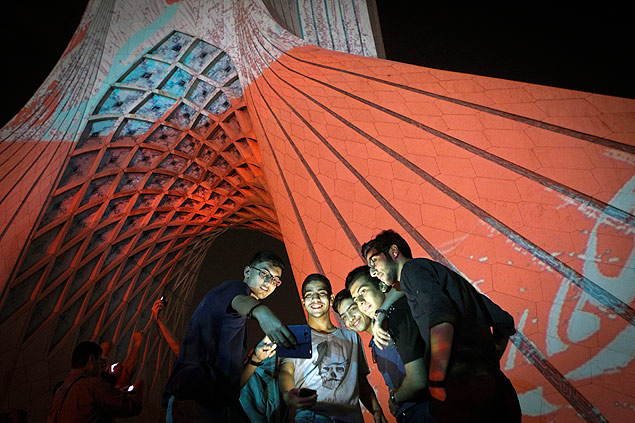 Garotos iranianos tiram selfies ao lado da nova instalação luminosa da torre Azadi, na capital, Teerã 