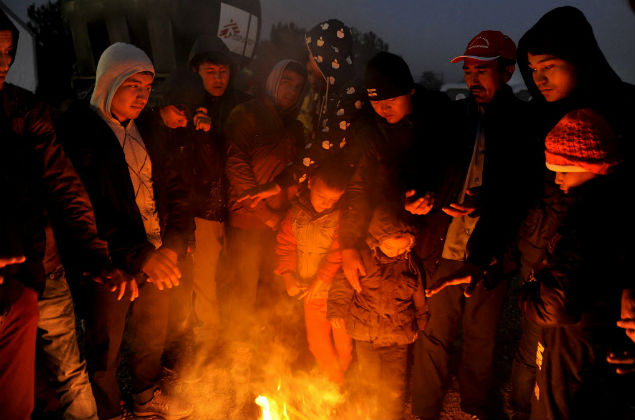 Refugiados e imigrantes se esquentam ao redor de fogueira perto da cidade de Idomeni