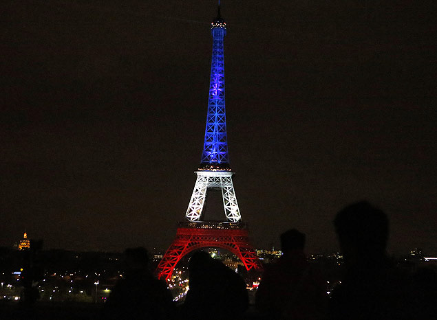 People watch the Eiffel Tower illuminated in the French national colors red, white and blue in honor of the victims of the terror attacks last Friday in Paris, Monday, Nov. 16, 2015. France is urging its European partners to move swiftly to boost intelligence sharing, fight arms trafficking and terror financing, and strengthen border security in the wake of the Paris attacks. (AP Photo/Frank Augstein) ORG XMIT: FAS118