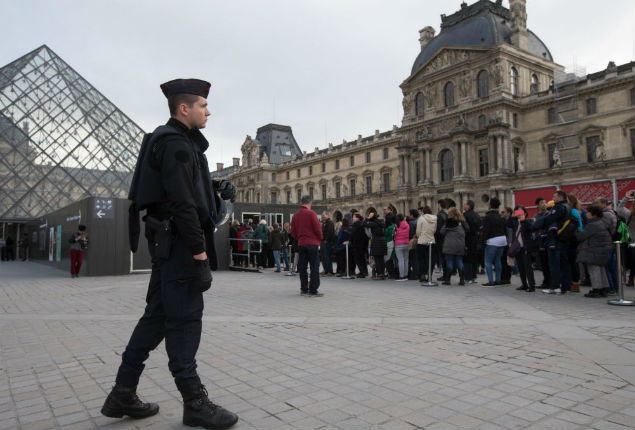 Policial ao lado de turistas no ptio do museu do Louvre