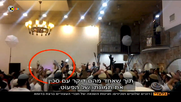 Reproduo de vdeo mostra judeus danando com armas na mo durante casamento; homem que aparece dentro de crculo vermelho estaria esfaqueando fotografia de beb palestino morto em ataque