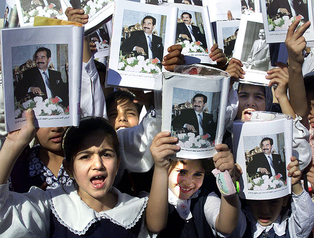 Crianas exibem livros escolares com fotografia de Saddam Husseim, em Bagd, no Iraque, em 2002