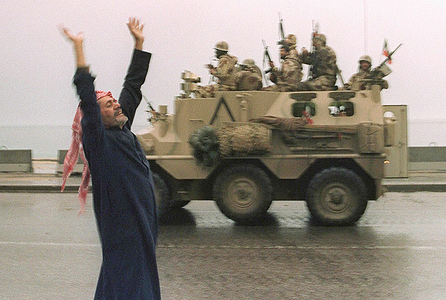 ORG XMIT: 210501_1.tif Guerra do Golfo: cidado do Kuait comemora fim da guerra, na Cidade do Kuait. (FILES): A Kuwaiti citizen raises his arms in celebration as a Saudi armoured personnel carrier passes on the street 27 February 1991 after allied forces rolled into Kuwait City the same day. The 10th anniversary of the Gulf War, when a US-led international coalition unleashed a war to liberate Kuwait from Iraqi occupation, is coming up 16 January 2001. AFP PHOTO/FILES/Bob PEARSON 