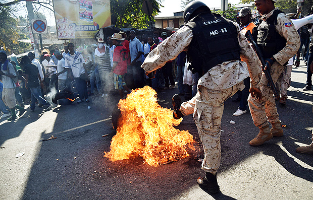 A Haitian policeman kicks a burning tire during clashes in a protest in Port-au-Prince, on January 19, 2016. Demonstrators are protesting against the presidential run-off and to demand a transitional government, denouncing fraud in the first round of presidential elections held October 25. Demonstrators blocked some streets with burning tires. The second round of presidential elections is scheduled for January 24 between ruling party candidate Jovenel Moise and Jude Celestin. Celestin has said he does not want to participate in the January 24 run-off against ruling party candidate Jovenel Moise, has yet to submit his official resignation to the Provisional Electoral Council(CEP). / AFP / HECTOR RETAMAL ORG XMIT: HR3448