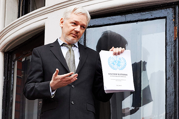 WikiLeaks founder Julian Assange addresses the media holding a printed report of the judgement of the UN's Working Group on Arbitrary Detention on his case from the balcony of the Ecuadorian embassy in central London on February 5, 2016. During a press conference on February 5 Julian Assange, speaking via video-link, called for Britain and Sweden to 