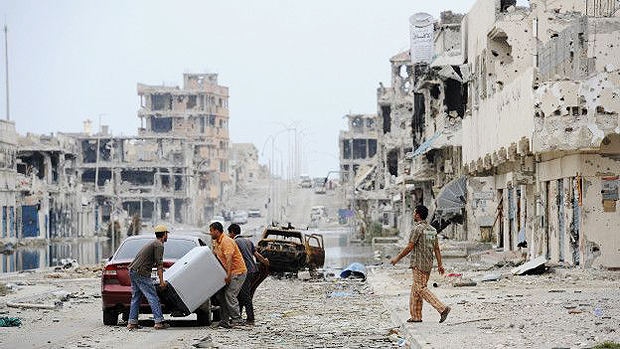 Homens carregam equipamento em rua da cidade de Sirte, que já foi bastante castigada pelos conflitos no país 