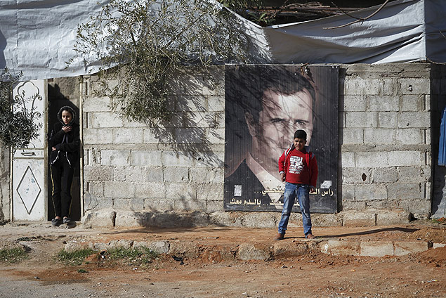Morador de rea controlada pelo governo srio ao lado de pster de Bashar al-Assad, em Damasco