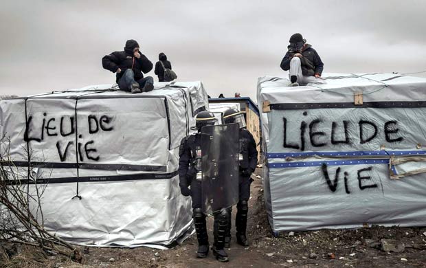 Policiais ao lado de imigrantes sobre telhados, em protesto ao desmonte do acampamento em Calais
