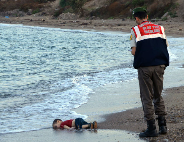 In this Wednesday, Sept. 2, 2015 file photo, a paramilitary police officer investigates the scene before carrying the body of 3-year-old Aylan Kurdi from the sea shore, near the beach resort of Bodrum, Turkey. A number of migrants are known to have died and some are still reported missing, after boats carrying them to the Greek island of Kos capsized. (AP Photo/DHA, File) TURKEY OUT ORG XMIT: NY471