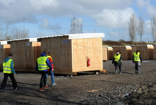 members walk past the France's first-ever refugee camp to meet international humanitarian for migrants and refugees on March 7, 2016 in Grande-Synthe, northern France. A second week of demolition was underway on March 7 in the Calais migrant camp known as the "Jungle" while France's first international-standard refugee camp was set to open further along the coast despite official opposition. Doctors Without Borders (MSF) has so far built a little over 200 of 275 planned cabins at the site to house at least 1,500 people -- many of whom are fleeing the demolition in Calais. The camp also has proper showers and toilets. / AFP / FRANCOIS LO PRESTI ORG XMIT: 1305 