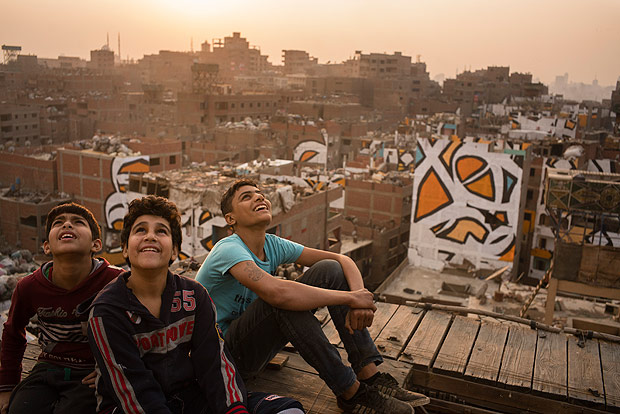 Boys watch pigeons fly from a coop as buildings painted with a mural by the artist eL Seed are seen in the distance, in the Manshiyat Naser district of Cairo, often associated with squalor, on March 17, 2016. The artist used the buildings as his canvas to celebrate the Egyptian capitals trash collectors, who are largely viewed as second-class citizens. (David Degner/The New York Times) ORG XMIT: XNYT55 ***DIREITOS RESERVADOS. NO PUBLICAR SEM AUTORIZAO DO DETENTOR DOS DIREITOS AUTORAIS E DE IMAGEM***