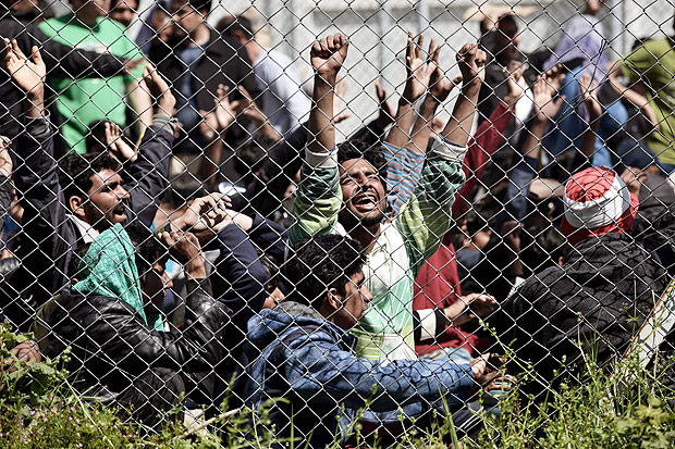 Men hold their hands up behind a chain link fence as Pakistani and Afghan migrants protest inside the Moria detention center in Mytilene on the Greek island of Lesbos on April 5, 2016 against deportation to Turkey. Migrant returns from Greece to Turkey begun on April 4 under the terms of an EU deal that has worried aid groups, as Athens struggles to manage the overload of desperate people on its soil. Over 51,000 refugees and migrants seeking to reach northern Europe are stuck in Greece, after Balkan states sealed their borders. Hundreds more continue to land on the Greek islands every day despite the EU deal. / AFP PHOTO / ARIS MESSINIS ORG XMIT: ARIS1794