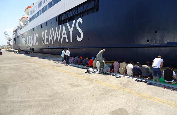 Refugiados muçulmanos se reunem para rezar diante de um navio de cruzeiro no porto de Pireus