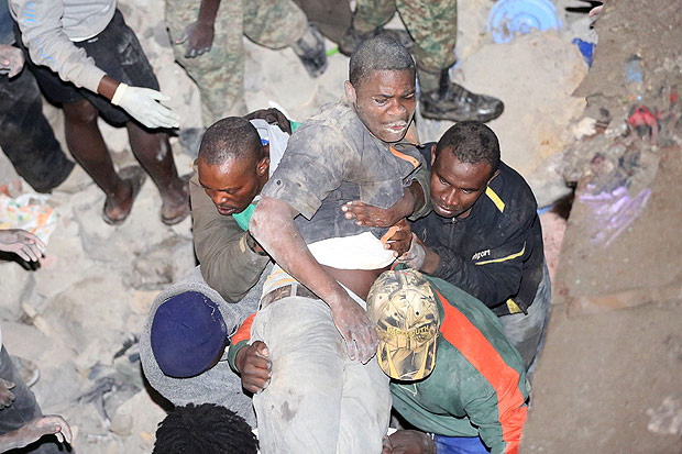 TOPSHOT - Kenyans carry a survivor rescued from a collapsed building in Nairobi late on April 29, 2016. At least seven people were killed when a six-storey building collapsed in the Kenyan capital amid torrential rainstorms, police said, as rescue teams shifted rubble in a desperate search for survivors. / AFP PHOTO / -