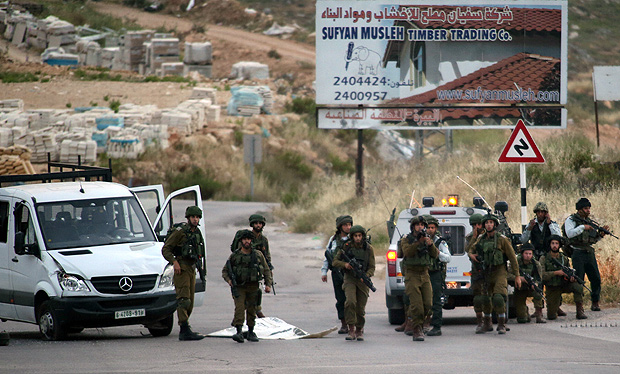 Soldados de Israel cercam o corpo de um palestino morto após atropelar militares na Cisjordânia