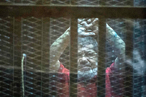 Egypt's ousted Islamist president Mohamed Morsi, wearing a red uniform, gestures from behind the defendant's bars during his trial at the police academy in Cairo on May 7, 2016. An Egyptian court recommended death sentences for six codefendants of Mohamed Morsi but not for the ousted Islamist president in their trial on espionage charges. / AFP PHOTO / KHALED DESOUKI ORG XMIT: KLD1898