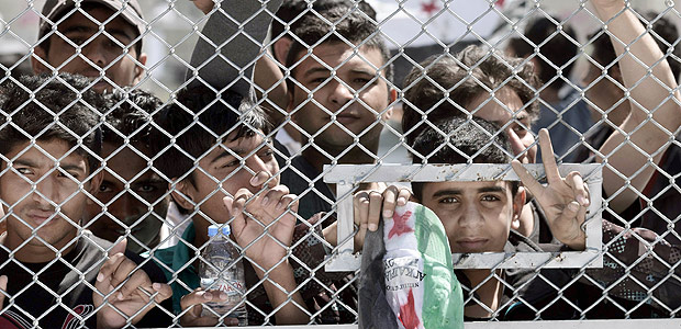 Um grupo de crianas imigrantes e refugiadas fica do lado da grade de um centro de deteno na Grcia