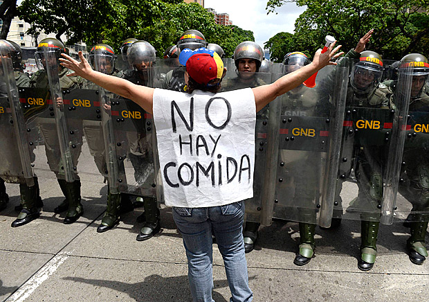 Manifestante protesta contra escassez que assola Venezuela em frente a policiais, em Caracas