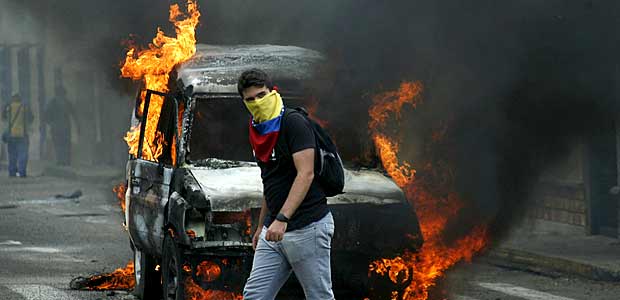 A demonstrator wearing a Venezuelan national flag to cover his face, walks in front of a burning van during a protest against President Nicolas Maduro's government in San Cristobal, Venezuela March 3, 2016. REUTERS/Carlos Eduardo Ramirez/File Photo FOR EDITORIAL USE ONLY. NO RESALES. NO ARCHIVE ORG XMIT: TOR906