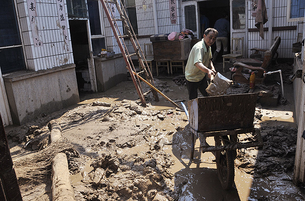 Homem limpa o quintal depois que uma enchente atingiu sua casa, na provncia de Hebei