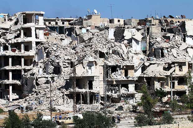 Syrians walk past heavily damaged buildings in the neighbourhood of Bani Zeid, on Aleppo's northern outskirts on July 29, 2016, as people come back to the previously rebel-held district, a day after Syrian government forces took control of it. Government forces have surrounded rebel-held districts in eastern Aleppo since July 17, sparking fears for an estimated 250,000 people who live there. / AFP PHOTO / GEORGE OURFALIAN