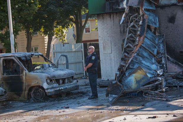 Policial protege posto de gasolina incendiado em meio aos protestos contra morte de suspeito por policial, em Milwaukee (EUA)