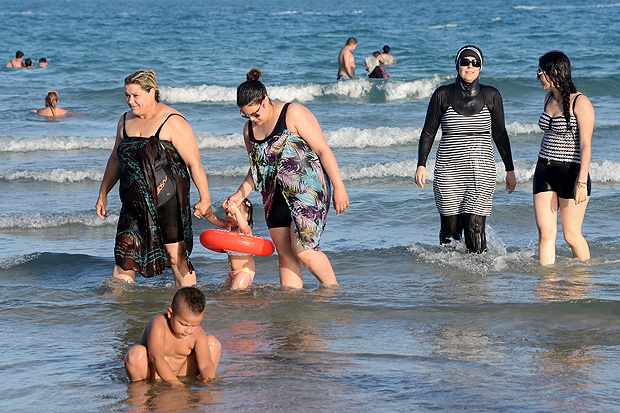Tunisian women, one (2ndR) wearing a "burkini", a full-body swimsuit designed for Muslim women, walk in the water on August 16, 2016 at Ghar El Melh beach near Bizerte, north-east of the capital Tunis. / AFP PHOTO / FETHI BELAID ORG XMIT: 3060