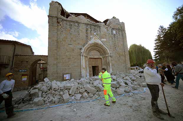 People stand in front of a damaged church in Amatrice on August 24, 2016 after a powerful earthquake rocked central Italy. The earthquake left 38 people dead and the total is likely to rise, the country's civil protection unit said in the first official death toll. Scores of buildings were reduced to dusty piles of masonry in communities close to the epicentre of the quake, which had a magnitude of between 6.0 and 6.2, according to monitors. / AFP PHOTO / FILIPPO MONTEFORTE ORG XMIT: FM7132