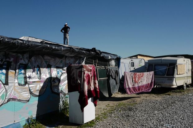A migrant stands on a roof in a makeshift camp in Calais, northern France, Tuesday, Aug. 23, 2016. Migrants from Sudan, Eritrea and elsewhere are camped by the thousand in the port city of Calais trying to reach Britain, where they believe they will have better job prospects. (AP Photo/Michel Spingler) ORG XMIT: SPIN103