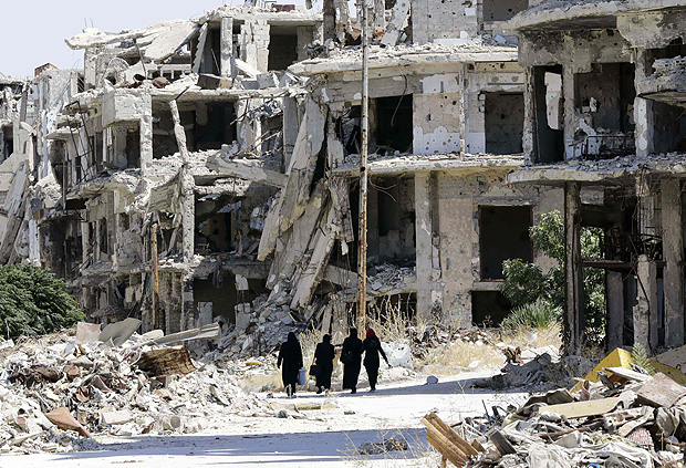 Mulheres srias caminham em meio a prdios destrudos em bairro controlado por Assad na cidade de Homs