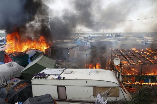 Fumaça e chamas no campo de refugiados de Calais, que está sendo desmontado pela França