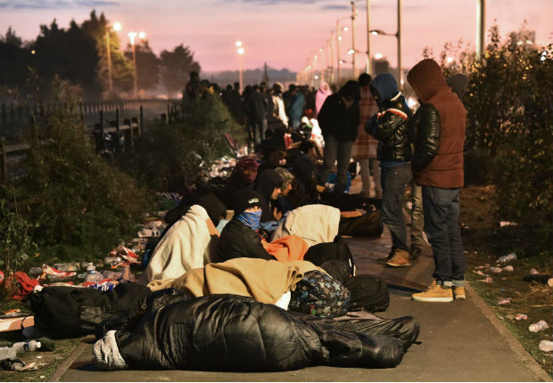 TOPSHOT - Migrants who slept outside an aid station queue to be assigned to one of the processing centres across France, near the "Jungle" migrant camp in Calais, northern France, on October 27, 2016, during a massive operation to clear the squalid settlement where 6,000-8,000 people have been living in dire conditions. / AFP PHOTO / PHILIPPE HUGUEN