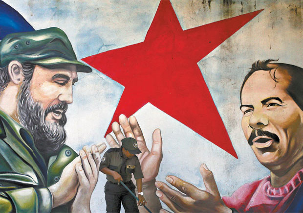 Nicaraguense varre diante de mural de Fidel Castro e Daniel Ortega em Mangua, Nicargua.