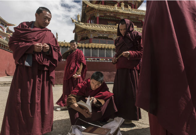 Monks check religious books for sale on the street in Larung Gar, China, Oct. 8, 2016. In Larung Gar, the world’s largest Buddhist institute, demolition teams are cutting through an extraordinary vista of hand-built red dwellings. (Gilles Sabrie/The New York Times) 