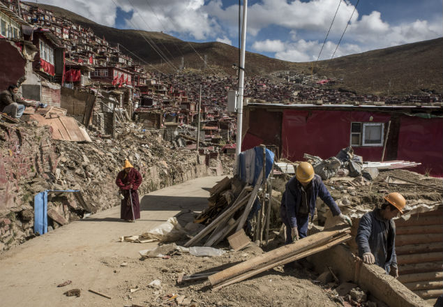 A Buddhist monk passes workers dismantling homes in Larung Gar, China, Oct. 8, 2016. China says the settlement is overcrowded and unsafe, but Tibetans claim the government’s aim is to weaken centers of power that can rival it. (Gilles Sabrie/The New York Times)