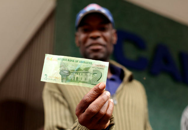 A man holds a two dollar note that he withdrawn at Cabs Bank in Harare central business centre on November 28, 2016. Zimbabwe will issue "bond notes" equivalent to the US dollar from next week to ease critical cash shortages, the central bank announced despite widespread public fear of a return to hyperinflation. / AFP PHOTO / Wilfred Kajese