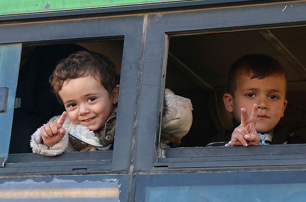 Syrian children, who were evacuated from rebel-held neighbourhoods in the embattled city of Aleppo, gesture as they arrive in the opposition-controlled Khan al-Aassal region, west of the city, on December 15, 2016, the first stop on their trip, where humanitarian groups will transport the civilians to temporary camps on the outskirts of Idlib and the wounded to field hospitals. Hundreds of civilians and rebels left Aleppo under an evacuation deal that will allow Syria's regime to take full control of the city after years of fighting. / AFP PHOTO / Baraa Al-Halabi
