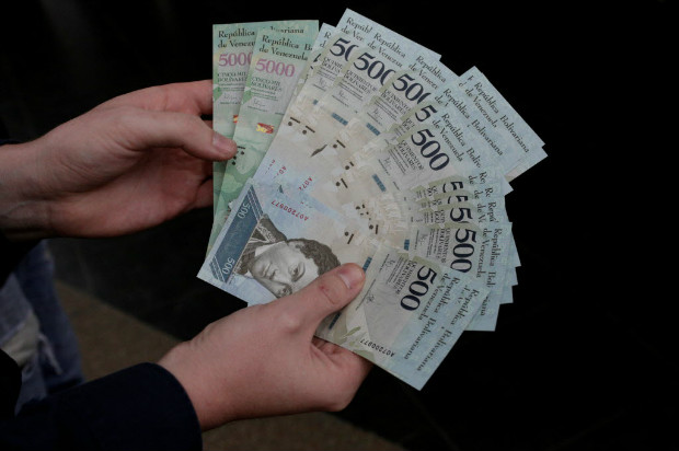 Homem segura notas de 500 e 5.000 bolvares, que pertencem  nova famlia da moeda, nesta segunda