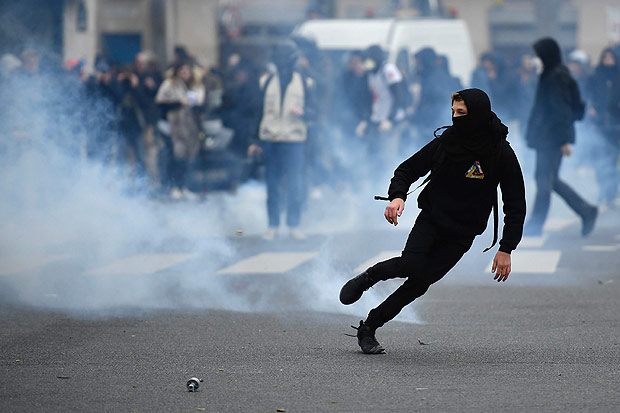TOPSHOT - A young man runs away from tear gas launched by riot police during a protest of students against police brutality, following the alleged rape of Theo, next to the "Lycee Voltaire" secondary school in Paris, on February 23, 2017. / AFP PHOTO / Lionel BONAVENTURE