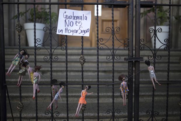 A sign that reads in Spanish: "Guatemala is not a safe home," hangs from the front gate of Presidential House above an artists' installation made of charred-stained dolls, in remembrance of the victims of a fire at a youth children, in Guatemala City, Thursday, March 9, 2017. Hospital officials say the death toll in the Wednesday morning fire at the Virgin of the Assumption Safe Home has risen to 28 after several more girls died overnight of severe burns. (AP Photo/Luis Soto)
