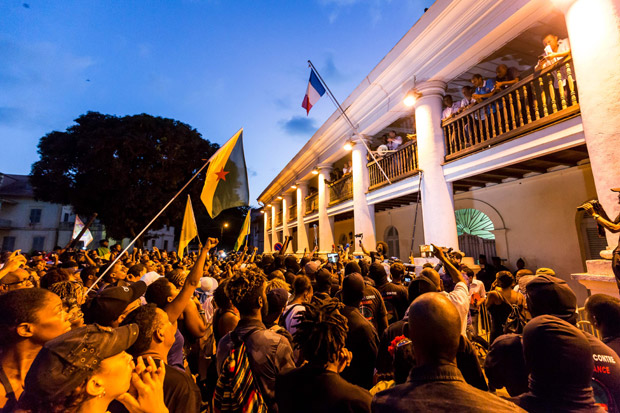 Guiana workers union secretary general Davy Rimane (on balcony) addresses the crowd on April 2, 2017 in Cayenne, French Guiana. France on April 1 announced a billion euros (USD 1,07 billion) aid for strike-hit French Guiana, as representatives of the Guianese told visiting ministers the South American territory should be given "special status". The vast South American territory, which is administered as a region of France, has been in the grip of labour unrest for the past 10 days. / AFP PHOTO / jody amiet
