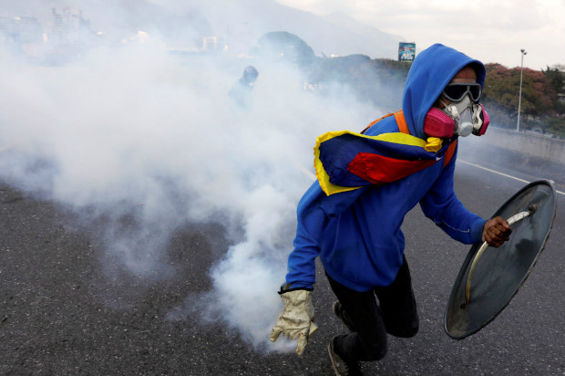 Manifestante encapuzado joga de volta bomba de gs lacrimogneo atirada pela polcia em protesto