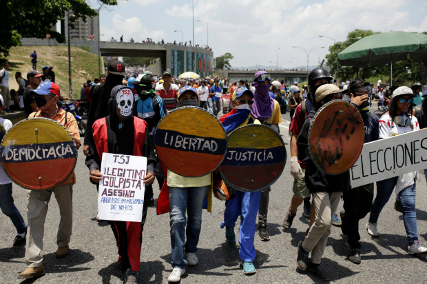 Encapuzados carregam escudos com as cores da bandeira venezuelana em protesto em Caracas