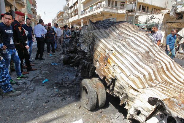 Iraquianos observam veículo destruído após explosão de carro-bomba na capital, Bagdá, nesta terça (30)
