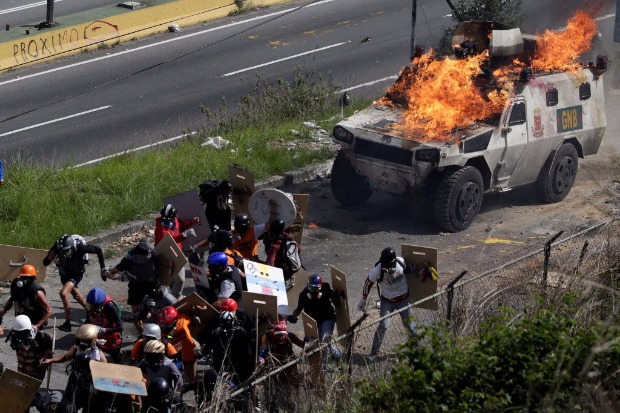 Manifestantes mascarados ateiam fogo em blindado da polícia durante confronto em Caracas