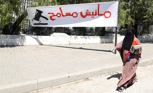 Mulher passa, em Tnis, na Tunsia, diante de faixa contrria  lei que protege acusados de corrupo 