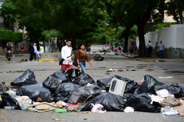 Venezuelanos caminham ao lado de barricadas de lixo em Caracas