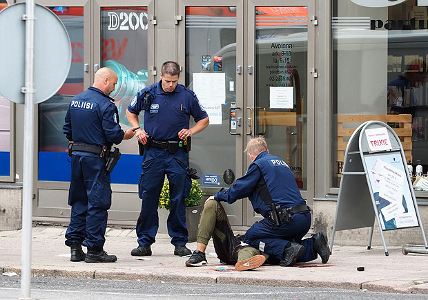 TOPSHOT - Police officers stand next to a person lying on the pavement in the Finnish city of Turku where several people were stabbed on August 18, 2017. Several people were stabbed in the southwestern Finnish city of Turku, police said after shooting and arresting a suspect. Public television station Yle reported that central Turku was on lockdown, with witnesses saying they had seen bodies lying on the ground in a busy area of the town. Businesses were shut. / AFP PHOTO / Kirsi Kanerva